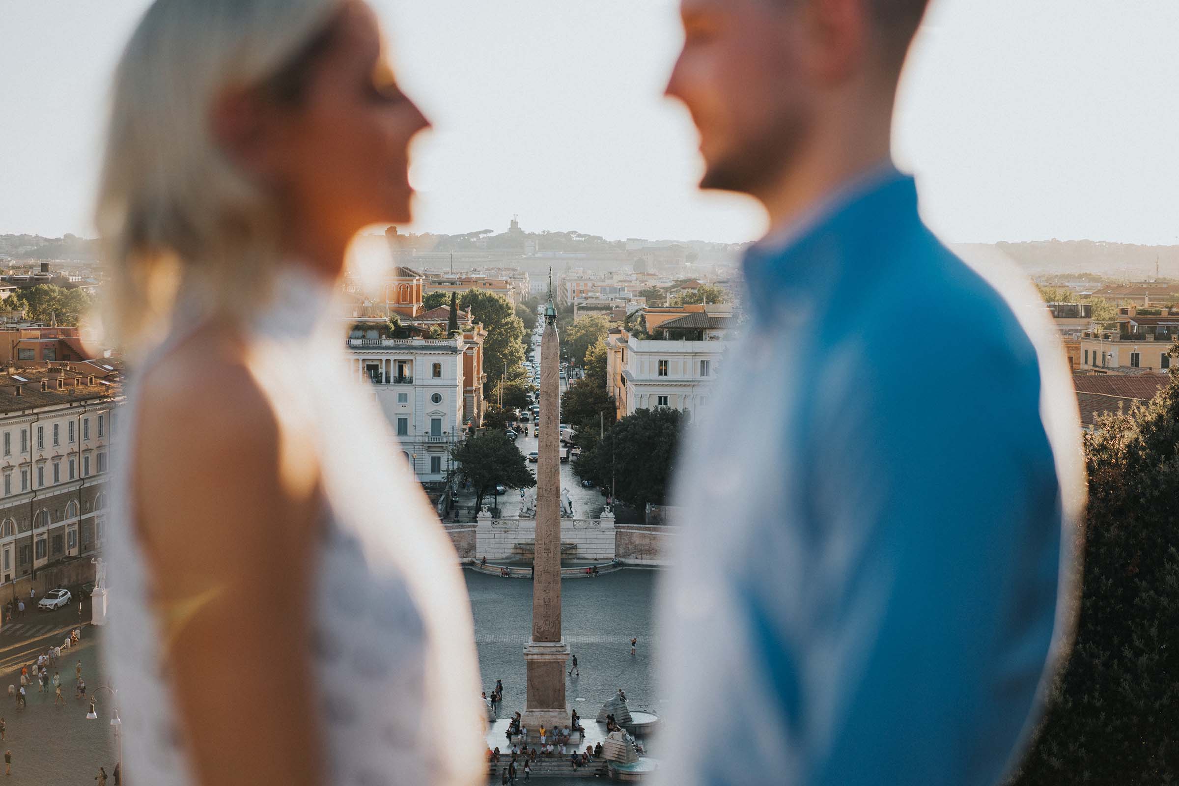 couple out of focus in foreground with obelisk behind them in Rome