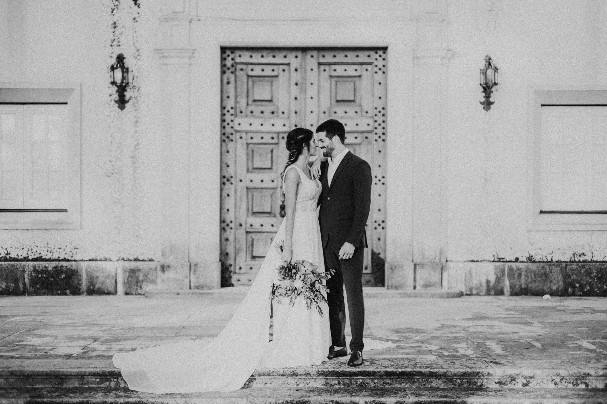 couple smiling in front of an oak door black and white