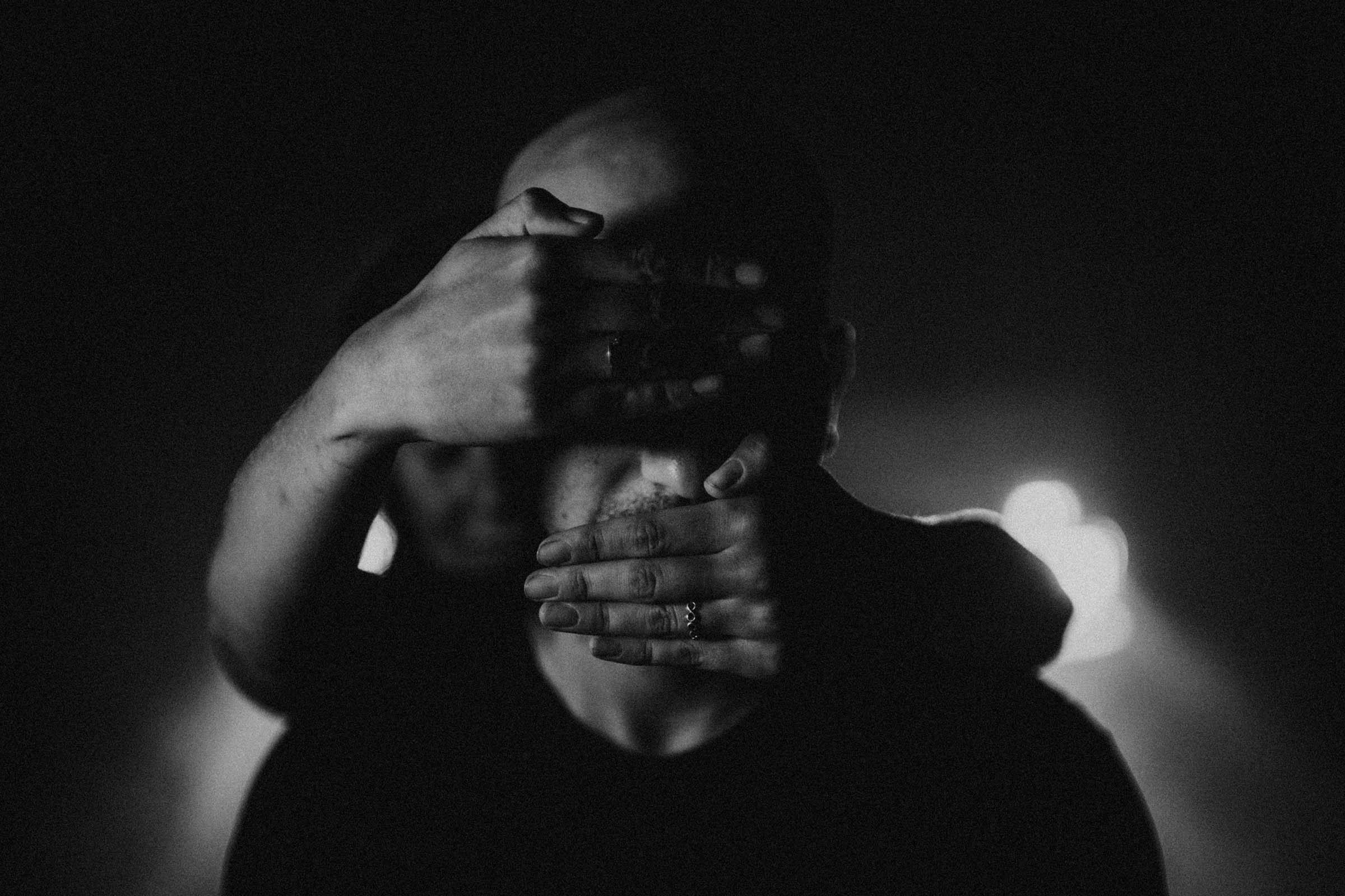 moody black and white photo grooms face covered by hands